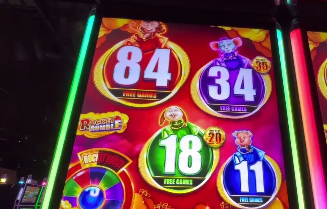 The four Must-Hit-By FREE GAMES counters on the glass: Red 89 (Mega, hits by 100), Purple 28 (Major, hits by 35), Green 16 (Minor, hits by 20), Blue 9 (Mini, hits by 15). The little spinning wheel bottom-left is the Rocket Boost decoy — ignore it.