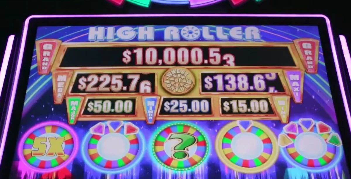 The read lives at the top: the HIGH ROLLER jackpot ladder and the row of five Wheel Spin prizes above the reels — here a 5X multiplier wheel (left) and the green ? Mystery wheel (center).